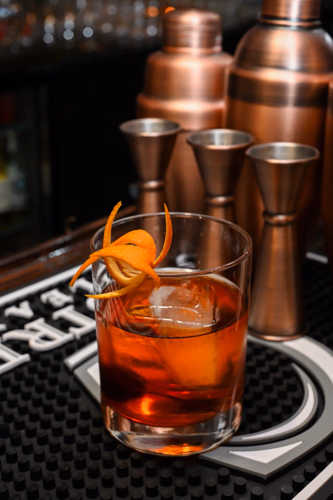 A warmly lit cocktail and sushi on a dark table
