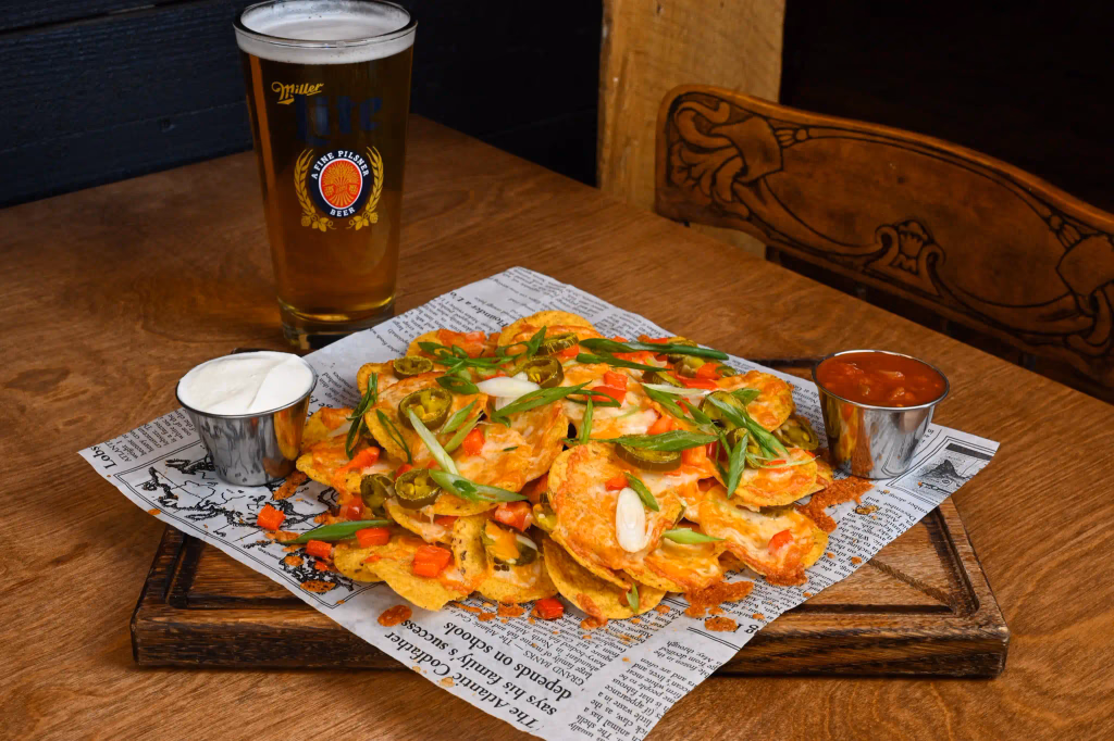 Loaded nachos served on a wooden table beside a beer